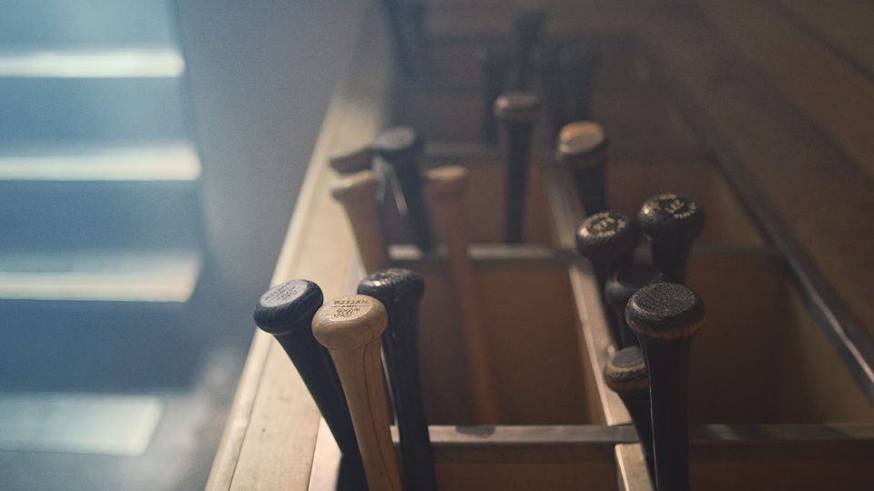 A rack of baseball bats standing in shafts of window light, shallow focus, dust in the air