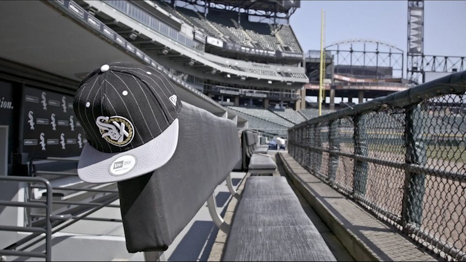 A White Sox cap resting on a rail as the hero of the frame, stadium ironwork and chain link behind it